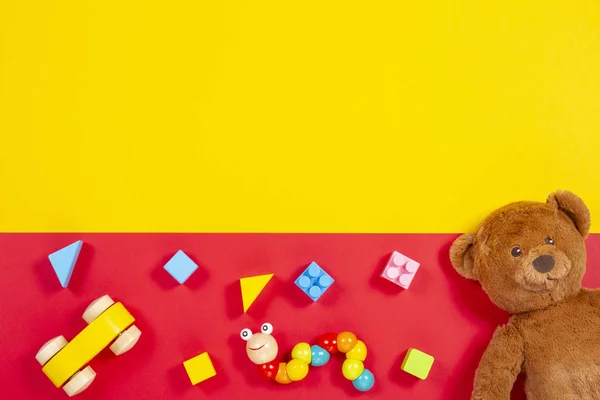Bebé niños juguetes fondo. Osito de peluche, coche de madera, ladrillos de colores sobre fondo rojo y amarillo — Foto de Stock