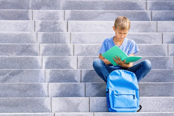 Jongen lezen boek zittend op de trap buiten — Stockfoto