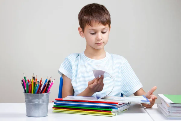 Menino sentado na mesa com pilha de livros escolares e cadernos e fazendo lição de casa em casa — Fotografia de Stock