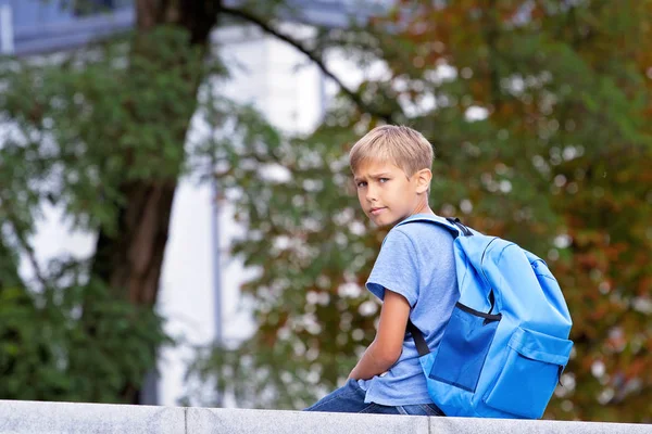 Niño sentado cerca de la escuela, vista trasera, se da la vuelta y mira en la cámara — Foto de Stock