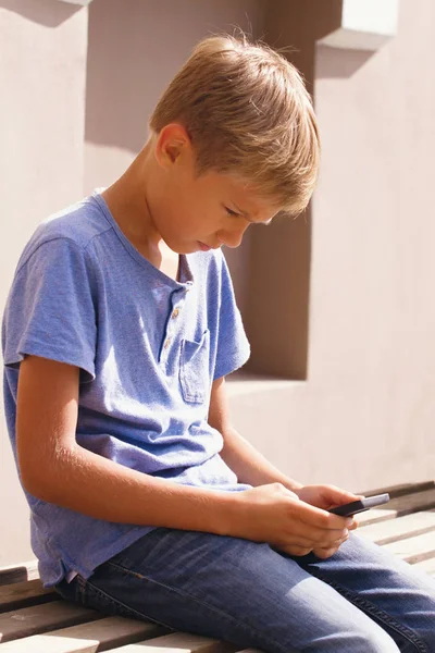 Menino com smartphone sentado nas escadas ao ar livre. Kid assistindo a tela, lendo, digitando, jogando jogos — Fotografia de Stock