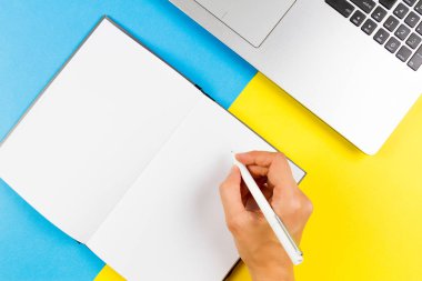 Kadın el not defterinde mavi ve sarı arka plan üzerinde yazma. Üstten Görünüm