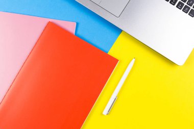 Mavi ve sarı renk arka plan üzerinde dizüstü bilgisayar, kağıt defter ve beyaz kalem Üstten Görünüm