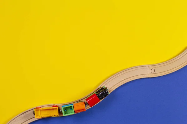 Tren de juguete y rieles de madera sobre fondo amarillo y azul — Foto de Stock