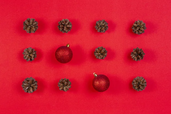 Composición navideña. Patrón hecho de conos de pino y decoración de Navidad roja sobre fondo rojo. Vista superior, plano — Foto de Stock
