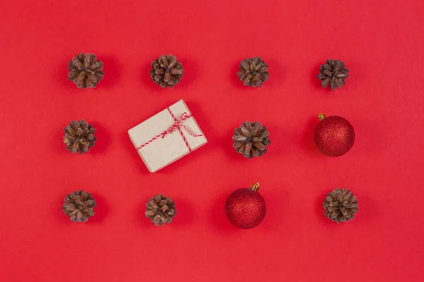 Composición navideña. Patrón hecho de conos de pino, decoración de Navidad y caja de regalo sobre fondo rojo. Vista superior, plano — Foto de Stock