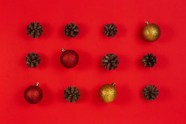 Composición navideña. Patrón hecho de conos de pino, decoración de Navidad amarilla y roja sobre fondo rojo. Vista superior, plano — Foto de Stock