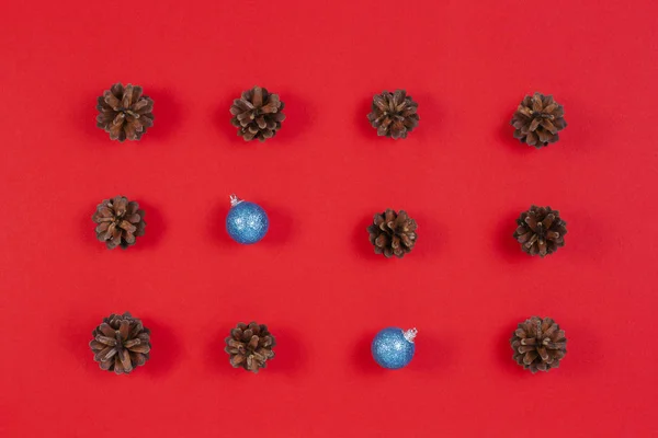 Composición navideña. Patrón hecho de conos de pino y decoración de Navidad azul sobre fondo rojo. Vista superior, plano — Foto de Stock