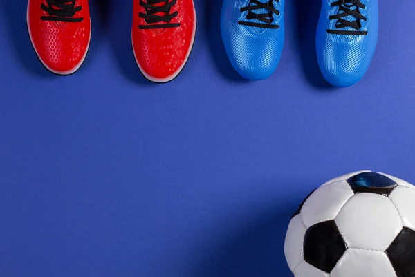 Soccer football background. Top view of soccer ball and two pair of soccer football sports shoes on blue background