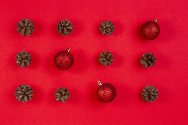Composición navideña. Patrón hecho de conos de pino y decoración de Navidad roja sobre fondo rojo. Vista superior, plano — Foto de Stock