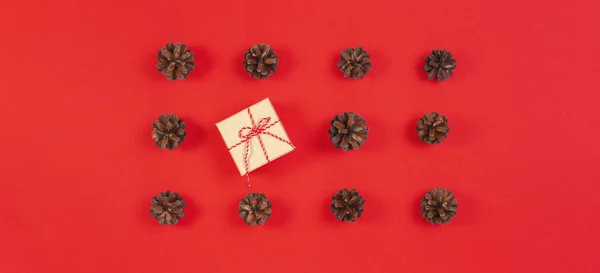 Composición navideña. Patrón hecho de conos de pino, caja de regalo de decoración de Navidad sobre fondo rojo. Vista superior, plano — Foto de Stock