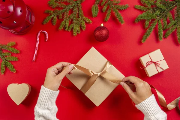 Karácsonyi ajándék csomagolás. Womans kezében karácsonyi csomagolás jelen háttér piros tábla mezőjében — Stock Fotó