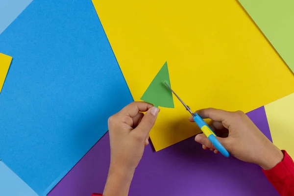 Close up de crianças mãos cortando árvore de Natal de papel colorido para preparar decorações de Ano Novo artesanal ou cartão — Fotografia de Stock