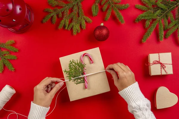 Empacotamento de presentes de Natal. Mãos das mulheres embalagem caixa de presente de Natal no fundo da mesa vermelha — Fotografia de Stock