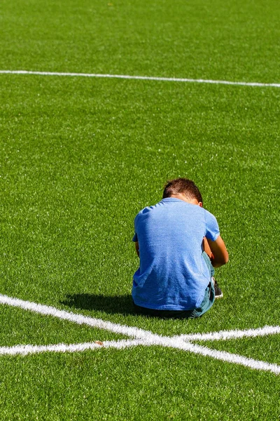 Droevig teleurgesteld jongen zittend op het gras in stadion — Stockfoto