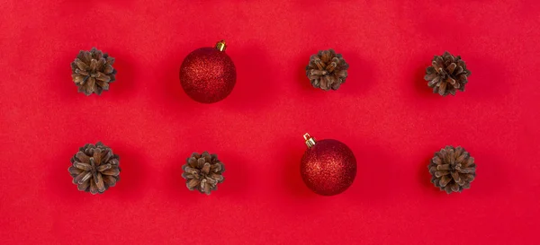 Composição de Natal. Padrão feito de cones de pinho e decoração de Natal vermelho no fundo vermelho. Vista superior, flat lay — Fotografia de Stock