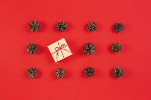 Composición navideña. Patrón hecho de conos de pino, caja de regalo de decoración de Navidad sobre fondo rojo. Vista superior, plano — Foto de Stock