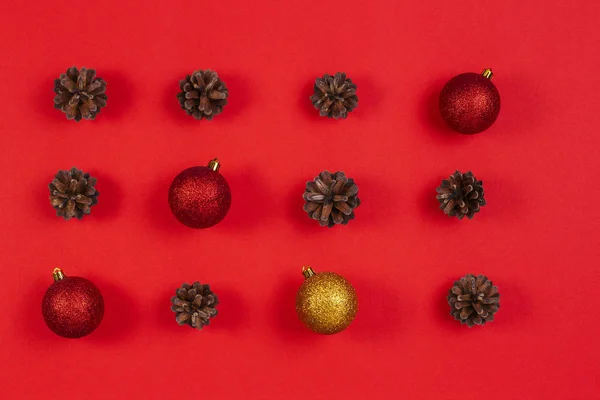 Composición navideña. Patrón hecho de conos de pino, decoración de Navidad amarilla y roja sobre fondo rojo. Vista superior, plano — Foto de Stock