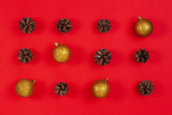 Composición navideña. Patrón hecho de conos de pino, decoración de Navidad amarilla y roja sobre fondo rojo — Foto de Stock