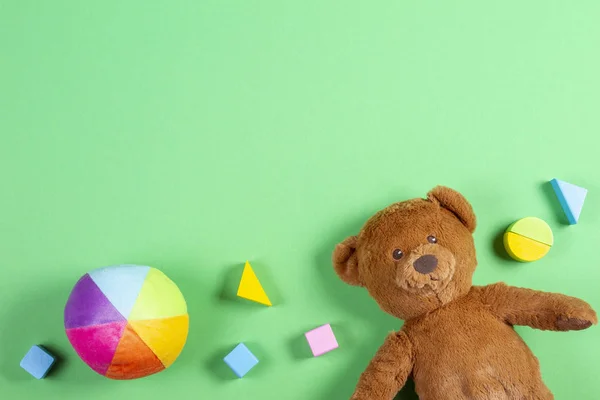 Crianças bebê brinquedos fundo com ursinho de pelúcia, cubos coloridos de madeira e tijolos no fundo verde — Fotografia de Stock