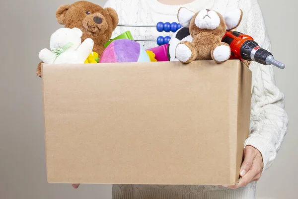 Scatola donazione mano donna con vestiti, giocattoli e libri — Foto Stock