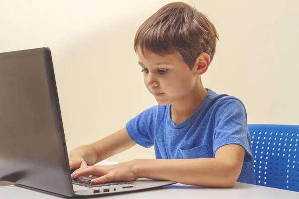 Menino concentrado sentado na mesa com computador portátil e fazendo lição de casa — Fotografia de Stock