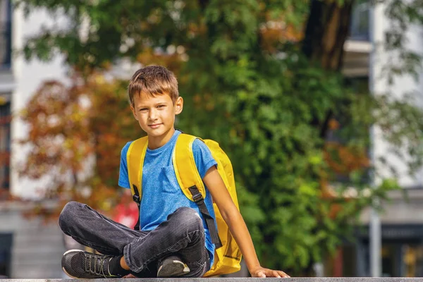 Mignon garçon intelligent avec sac à dos assis à l'extérieur après l'école . — Photo