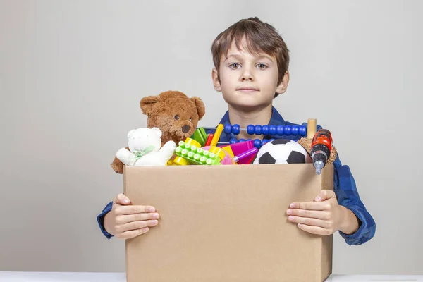 Donation-konceptet. Kid innehar donera låda med kläder, böcker, skolmaterial och leksaker — Stockfoto