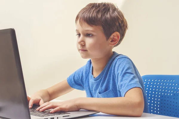 Menino concentrado sentado na mesa com computador portátil e fazendo lição de casa — Fotografia de Stock