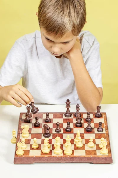 Miúdo a jogar xadrez. Rapaz a olhar para tabuleiro de xadrez e a pensar na sua estratégia . — Fotografia de Stock