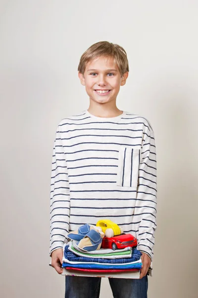 Concepto de donación. Niño sosteniendo en sus manos libros, ropa y juguetes para donar —  Fotos de Stock