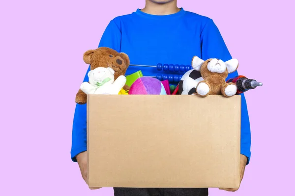 Koncept darování. Dítě drží darovat box s oblečení, knihy, školní potřeby a hračky, žlutou barvu pozadí — Stock fotografie