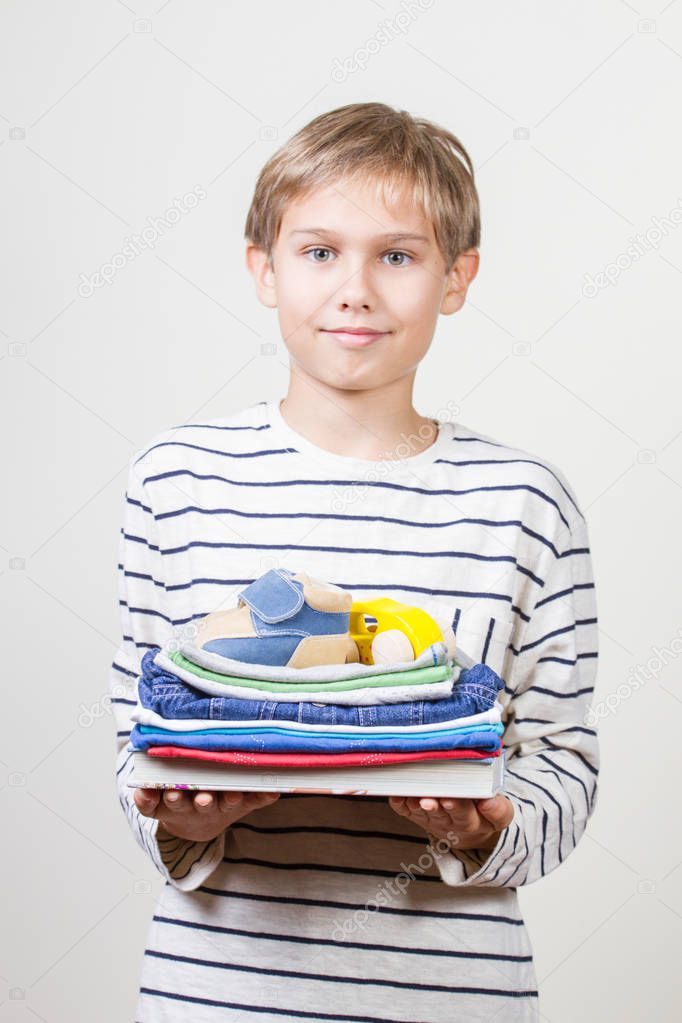 Donation concept. Kid holding in his hands books, clothes and toys for donate