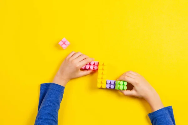 Kinderhände spielen mit bunten Plastiksteinen auf gelbem Hintergrund — Stockfoto