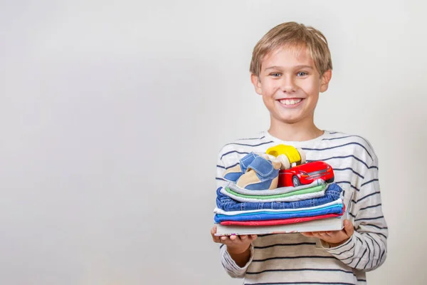 Concepto de donación. Niño sosteniendo en sus manos libros, ropa y juguetes para donar —  Fotos de Stock