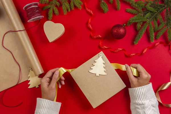 Christmas presentpapper. Kvinnans händer packning jul presenterar box på röda bordsbakgrund — Stockfoto