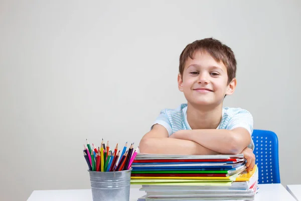 Niño sonriente con libros coloridos, cuadernos y libros de texto sentados a la mesa — Foto de Stock