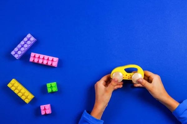 Child hands playing with wooden toy car on blue background — Stock Photo, Image