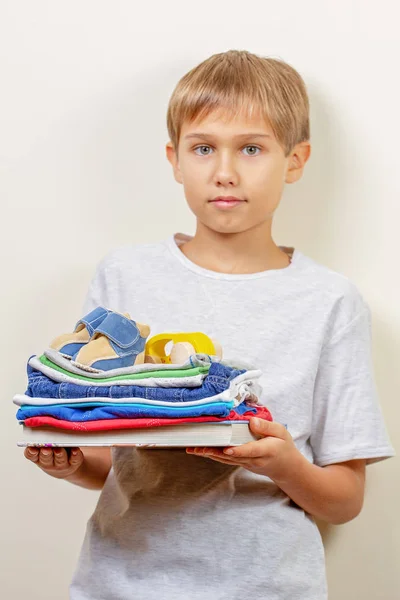 Conceito de doação. Kid segurando em suas mãos livros, roupas e brinquedos para caridade — Fotografia de Stock