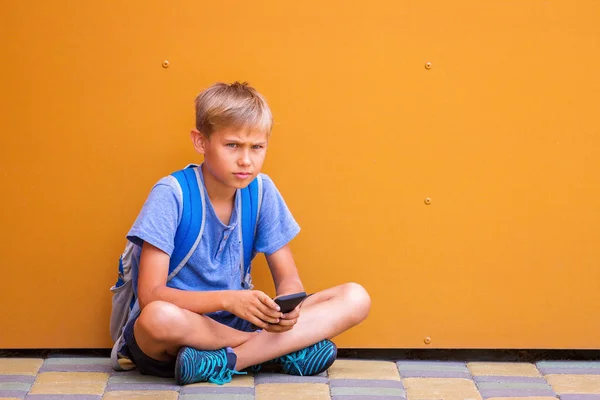 Menino com smartphone sentado no chão perto da parede colorida — Fotografia de Stock