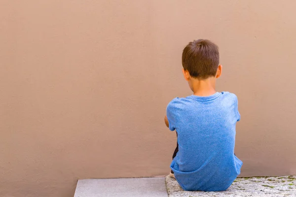 Triste chico solo sentado en el suelo detrás de la pared al aire libre — Foto de Stock