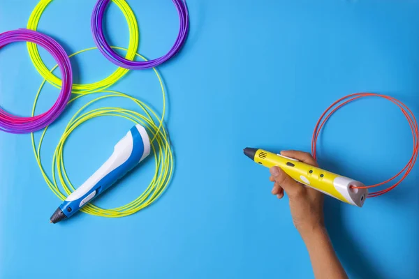 Kid mão segurando caneta 3d com filamento de plástico no fundo azul — Fotografia de Stock