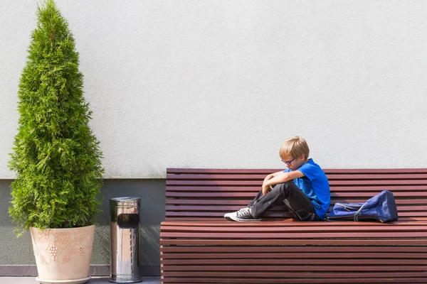 Ledsen, trött barn sitter ensam på bänken utomhus. — Stockfoto