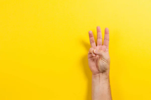 Ember kéz mutatja a három ujját sárga háttéren. Két szám szimbólum — Stock Fotó