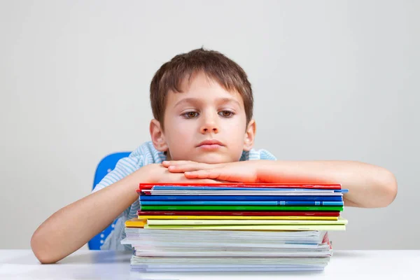 Écolier bouleversé assis au bureau avec une pile de livres scolaires et de cahiers — Photo