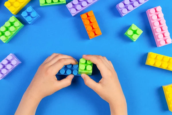 Kids hand playing with colorful plastic construction blocks on blue background — Stock Photo, Image