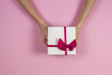 Tebrikler arka plan. Çocuk holding mevcut hediye kutusu ile şerit pembe bir arka plan üzerinde ellerini. Üstten görünüm. Mevcut Doğum günü, Sevgililer günü, Noel, yeni yıl