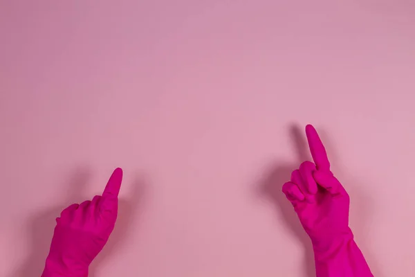 Las manos de mujer con guantes de goma apuntan hacia arriba con el dedo, sobre fondo rosa — Foto de Stock