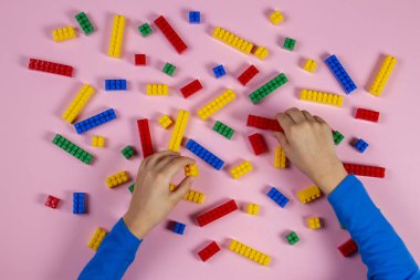 Çocuk pembe bir arka plan üzerinde renkli bina plastik tuğla ile oynarken ellerini. Eğitim gelişmekte olan oyuncaklar arka plan