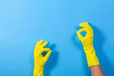 Sarı lastik eldivenli kadın elleri jest yapıyor. Tamam, mavi arka planda üst manzara.